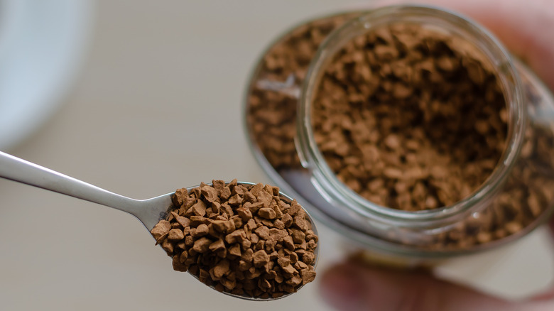 Instant coffee granules on spoon with a container in the background