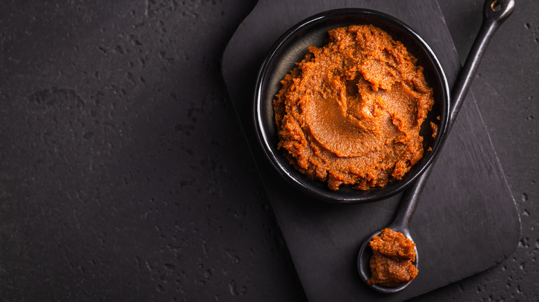 Red miso paste in black bowl laid on a black background with a black spoon