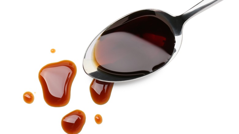 Soy sauce splashing off metal spoon on a white background