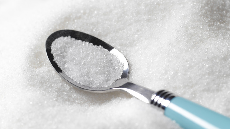 Caster sugar on a teaspoon nestled inside a heap of sugar