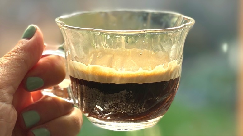 hand holding clear glass teacup half full with espresso shot