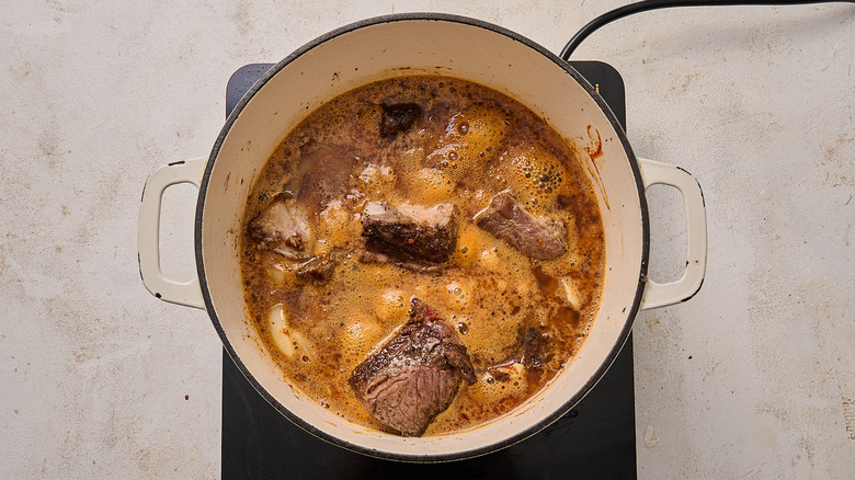 pouring beer into pot with short ribs