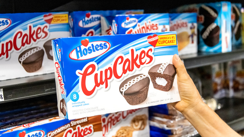 A person holding a package of Hostess Cupcakes in front of store shelves