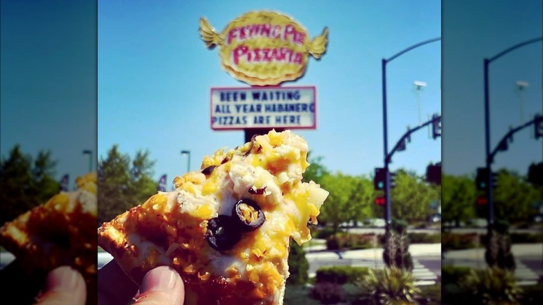Hand holding a slice of Habanero Pizza in front of Flying Pie Pizzaria sign