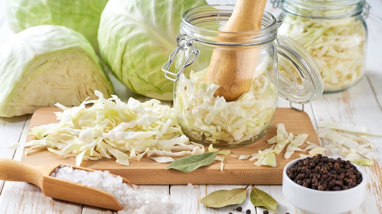 sliced green cabbage in a jar with cabbages, salt and peppercorns