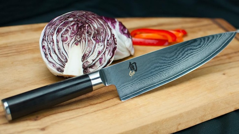 The Shun Western Chef's Knife on a wooden cutting board next to a head of cabbage