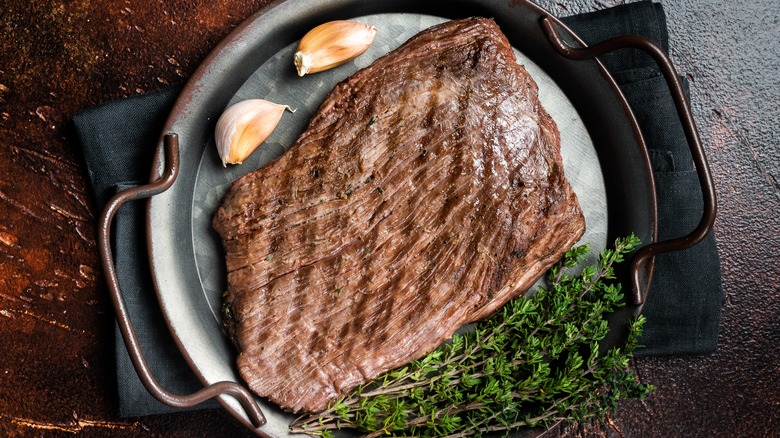 grilled flank steak in a pan with garlic and thyme