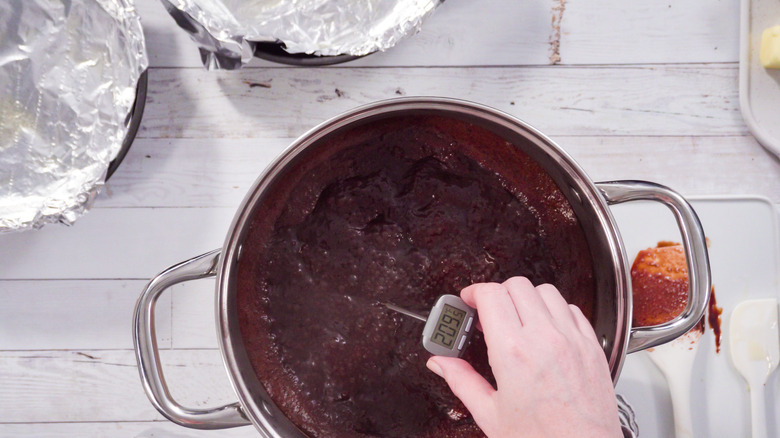 Hand holding thermometer in steel pot of cooking chocolate fudge