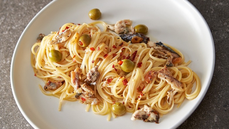 Spaghetti dish containing mackerel with oil, chili, and olives on white plate