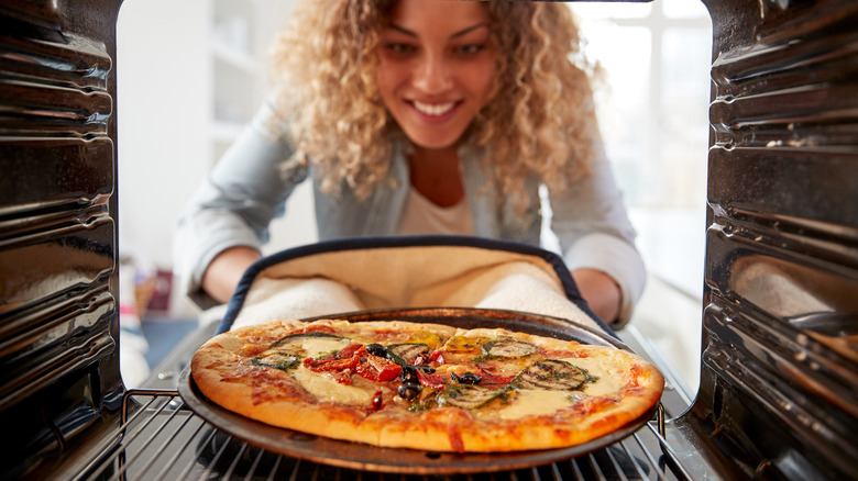 women putting pizza in oven