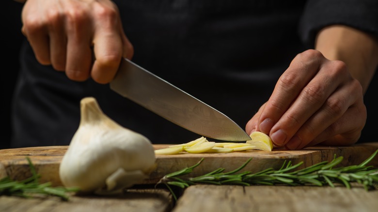 hands slicing garlic on wooden cutting board