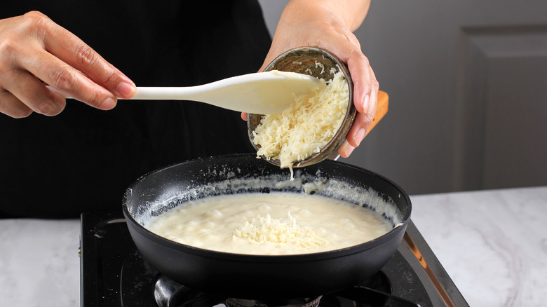 cook adding cheese to a sauce