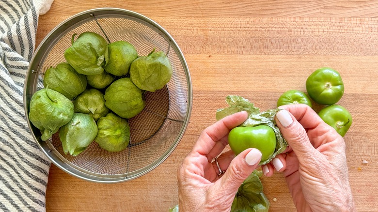 hand peeling husk off tomatillo