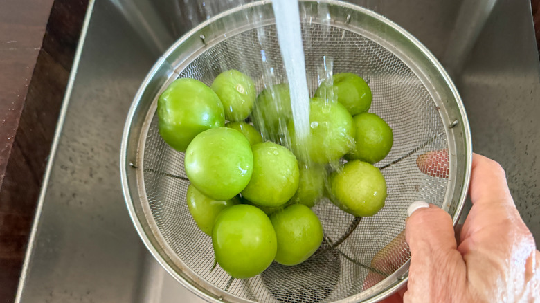 hand rinsing tomatillos under sink