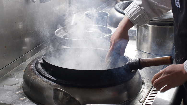 A person cleaning a wok with a wok brush. 