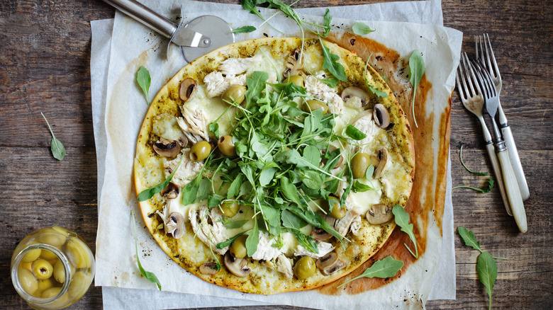 Pizza with arugula, olives, chicken, and mushrooms