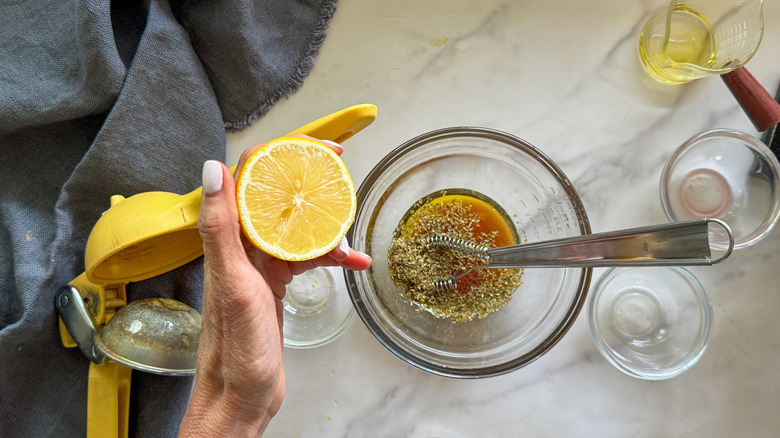 hand adding lemon to glass bowl of dressing ingredients