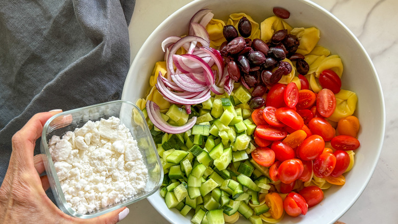 adding feta cheese to bowl of salad ingredients