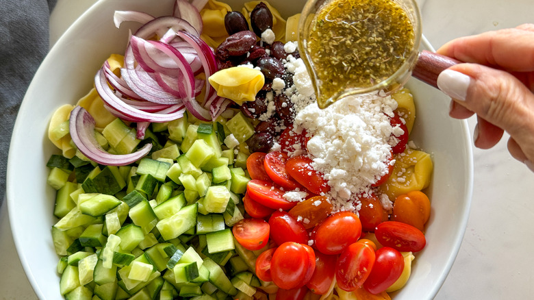 hand adding dressing to bowl of salad