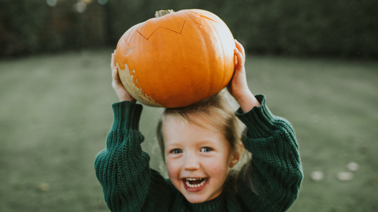 Smiling child holding a pumpkin outside