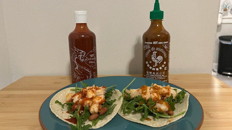 shrimp taco on plates with sriracha bottles in back