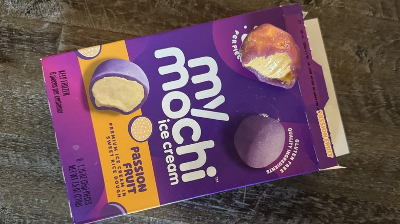 An opened box of My/Mochi passion fruit ice cream with one mochi bitten lying on top of box