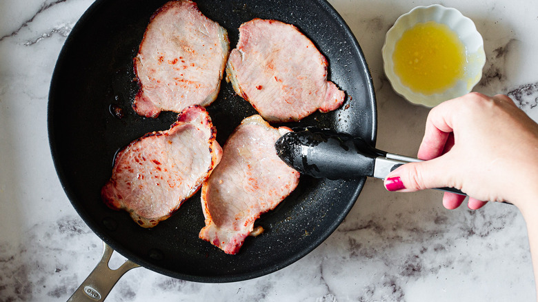 tongs flipping Canadian bacon in pan