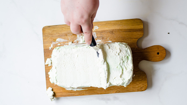 whipped cream mixture covering the spumoni ice cream cake on a wooden cutting board