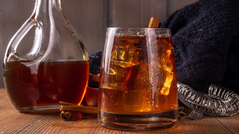 Jug of dark maple syrup beside a cocktail