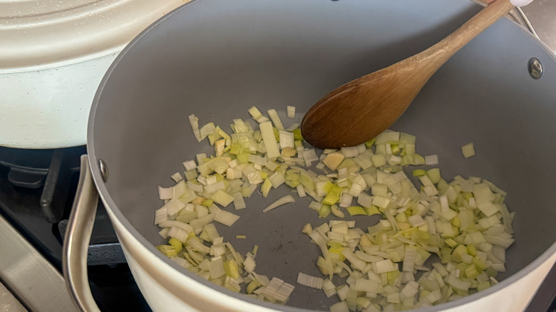 Wooden spoon stirring chopped leeks and garlic in pot
