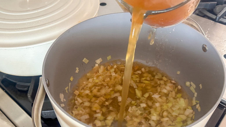 Broth pouring into pot with aromatics