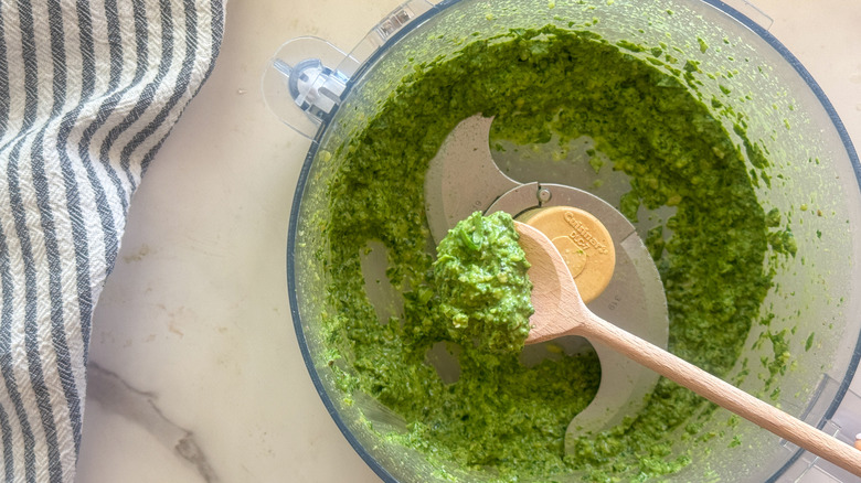Spoon with pesto over food processor with pesto