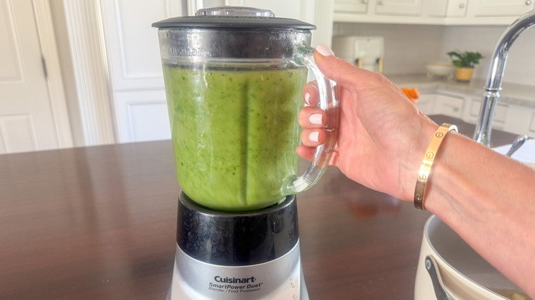 Green soup blending in blender with hand holding onto handle