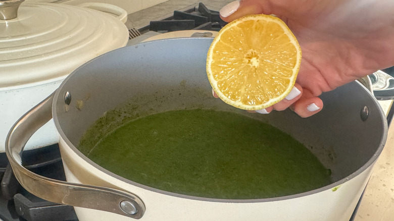Hand squeezing lemon into spinach soup