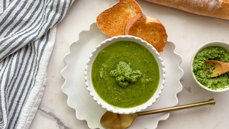 Bowl of spinach soup with bread slices and bowl of pesto