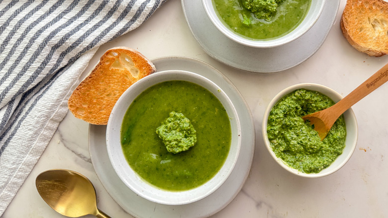 Bowl of spinach soup with slice of bread next to bowl of spinach pesto