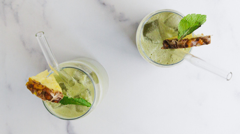 Two green drinks with garnishes and straws