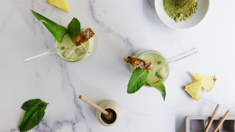 Overhead view of two drinks with garnishes and ingredients around