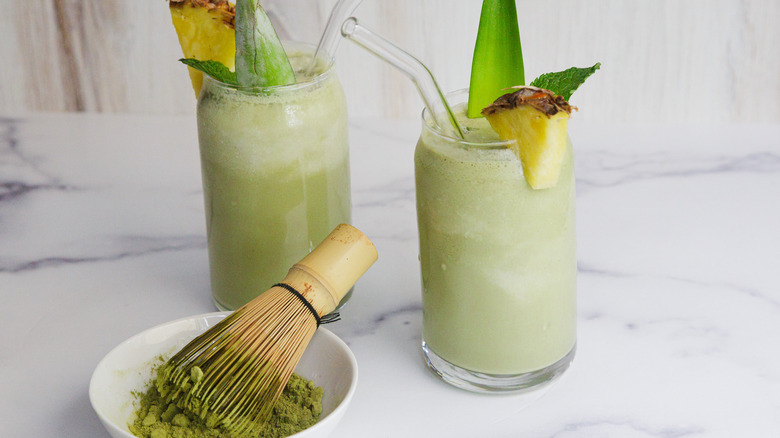 Two green drinks with matcha powder in a bowl