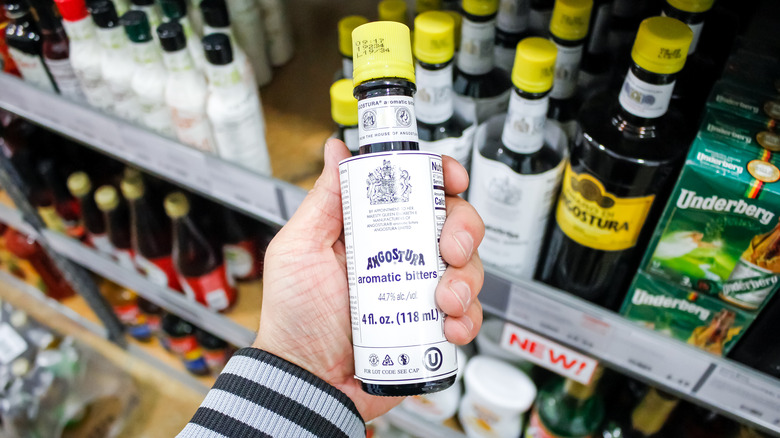 a man holds one bottle of bitters from a grocery shelf