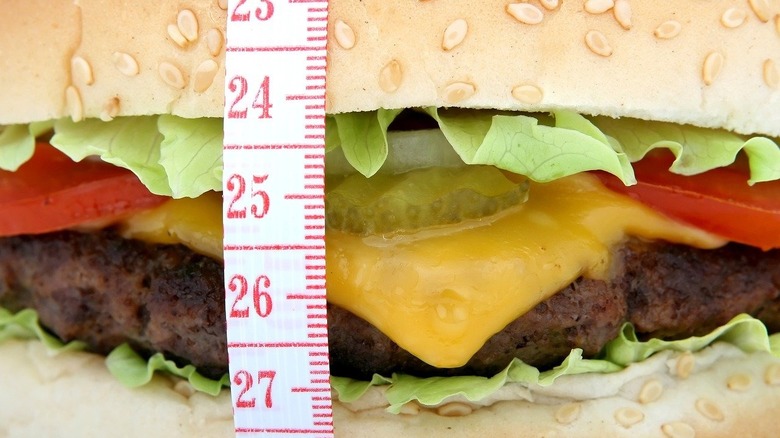 A cheeseburger with measuring tape around it