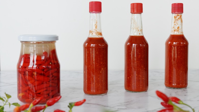 Unlabeled hot sauces beside jarred chilis