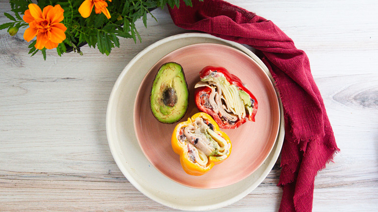 Two bell pepper sandwich halves on pink plate with avocado