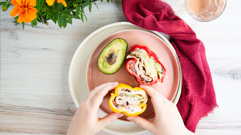 Hands holding bell pepper sandwich on pink plate with avocado