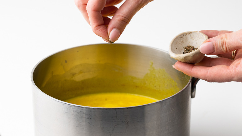 black pepper being added to saucepan