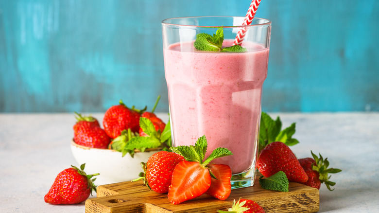 A strawberry smoothie in a glass with sliced berries and mint garnish