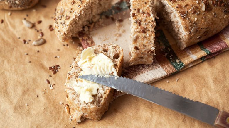 spreading butter on a slice of multigrain bread