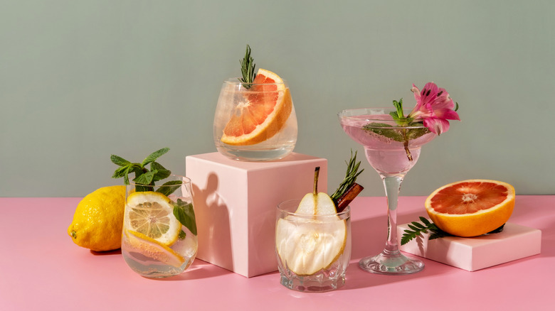 Four cocktails with fruits and garnishes piled around pieces of citrus