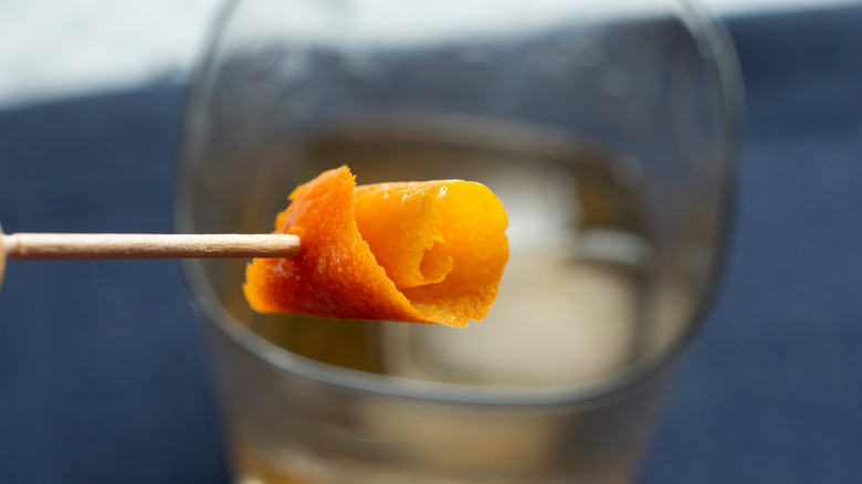 An orange rose garnish on a toothpick held up over a cocktail glass