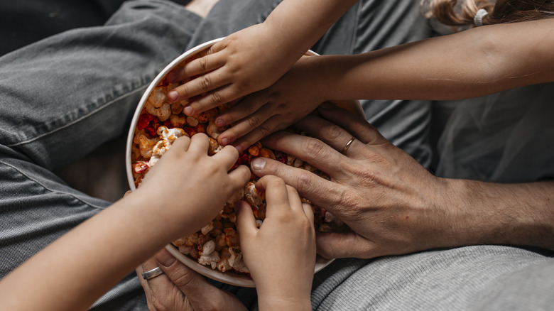 Several people's hands reaching into bowl of flavored popcorn